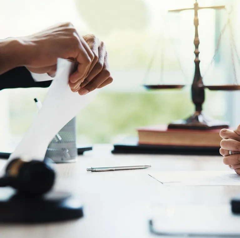Hands tearing a document on a desk with legal scales, books, and a pen nearby.