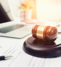 A wooden gavel rests on a desk with legal documents and a laptop, symbolizing justice and law.
