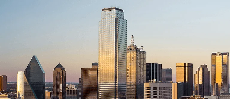 Panoramic view of Dallas skyline at sunset, featuring prominent skyscrapers like the glass-clad bank tower and distinctive triangular building.