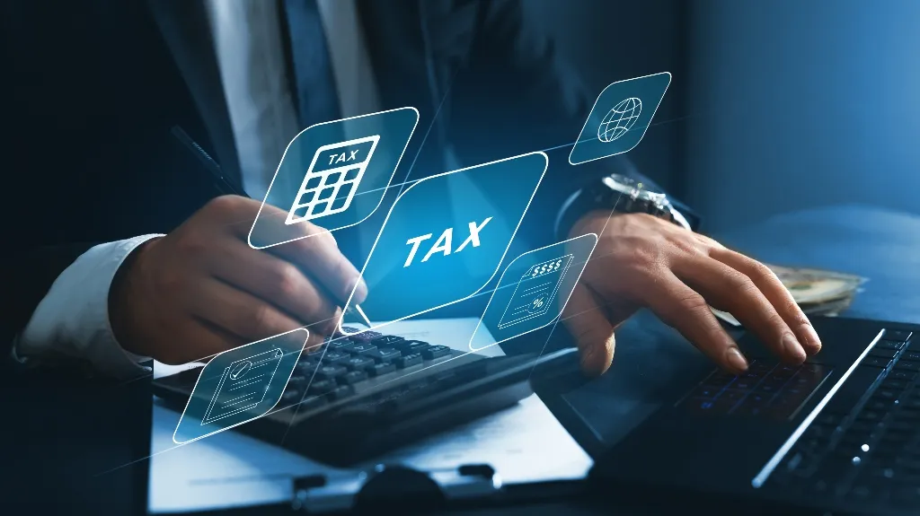 Person in business attire using calculator and laptop with digital tax icons overlay.