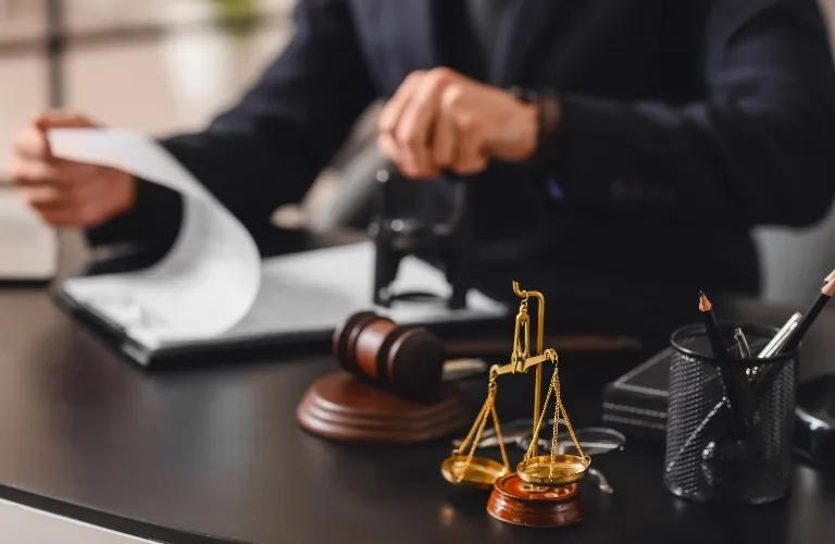 Golden scales of justice, wooden gavel, and person stamping documents on black desk.