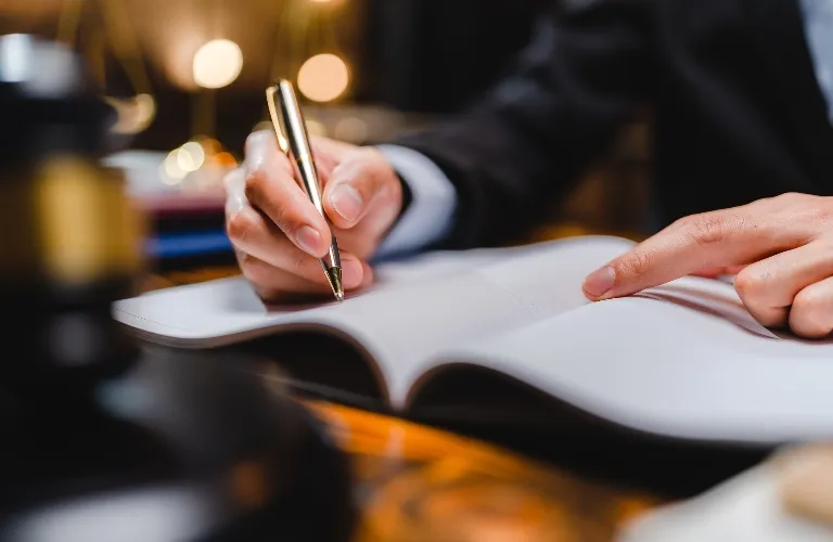 Close-up of a person in formal attire writing in an open book with a gold pen.