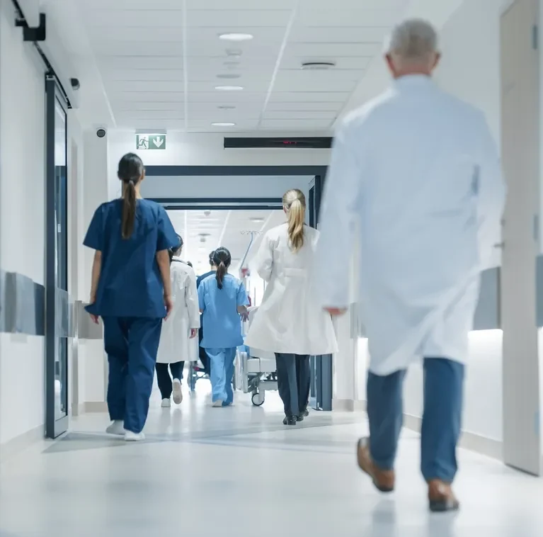 Medical professionals in white coats and scrubs walking down a bright hospital corridor.