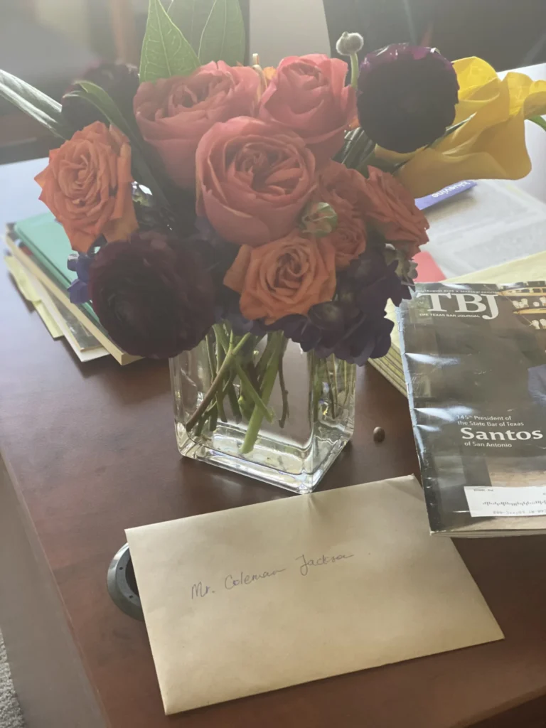 Vase with mixed roses and flowers on desk beside envelope and magazine titled "The Texas Bar Journal.