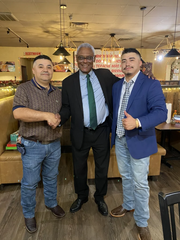 Three men posing in a restaurant with wooden floors and festive decorations.