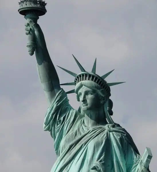 Close-up of the Statue of Liberty's upper torso, torch, and crown against a cloudy sky.