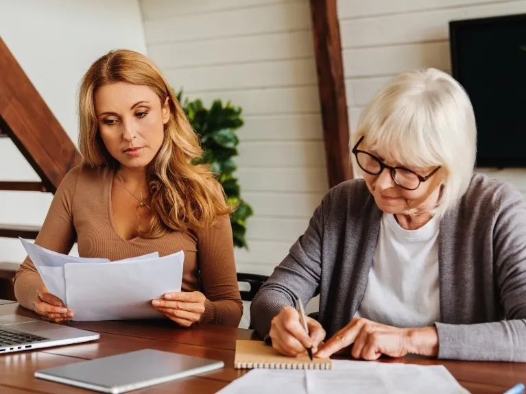 Two women, one younger and one older, reviewing documents at a wooden table.