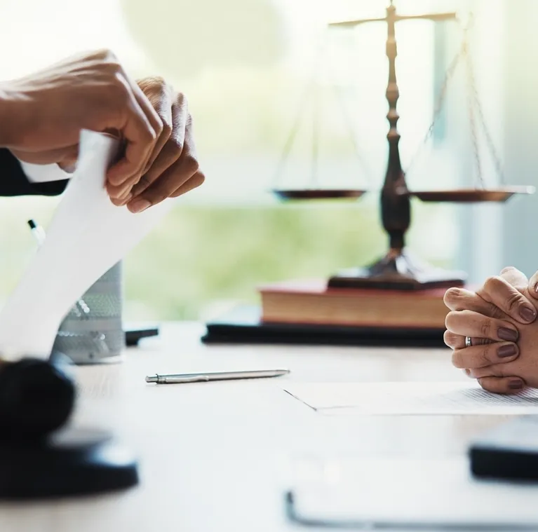 Two people at a desk with legal scales, documents, and a pen, engaged in discussion.