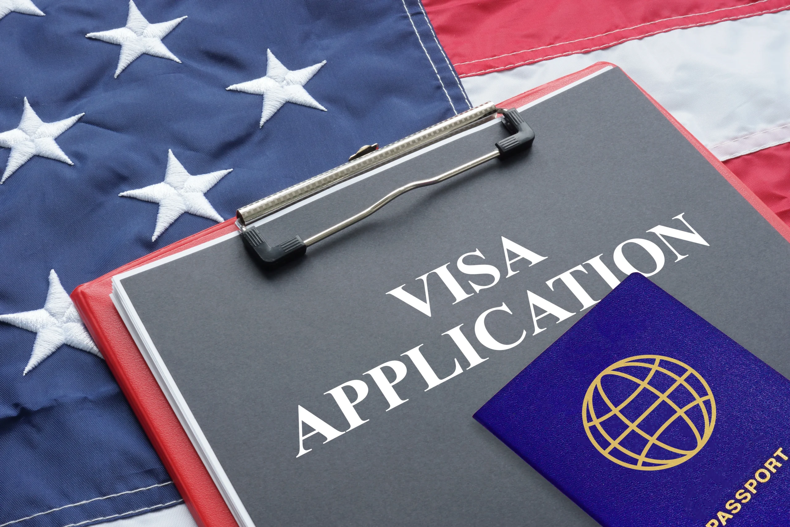 Clipboard with visa application form and passport on American flag background.