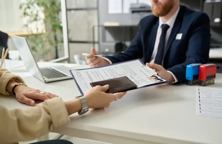 Professional man in suit reviewing documents with another person at office desk.