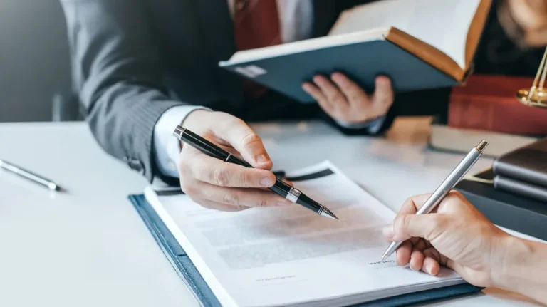 Two individuals in business attire reviewing and signing a document on a white table.
