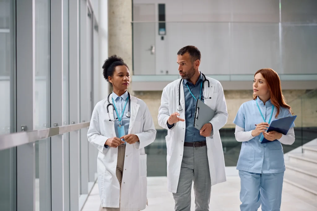 Three medical professionals walking and discussing in a modern hospital corridor.