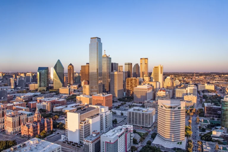 Aerial view of a city skyline with modern skyscrapers and clear blue sky at sunset.