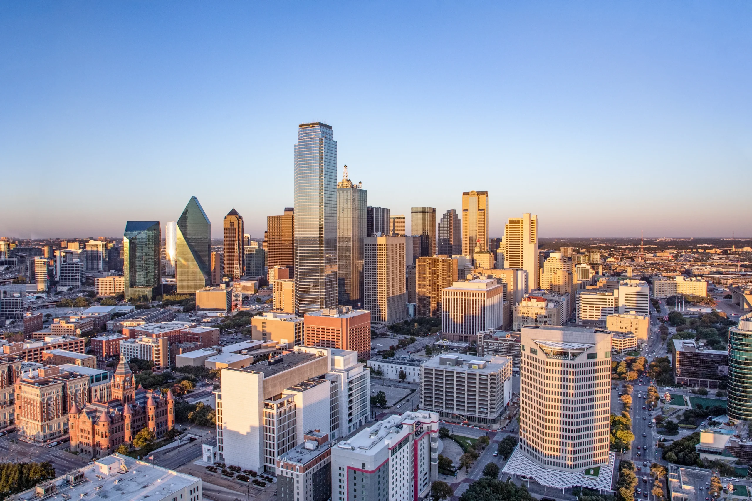 Aerial view of a city skyline with modern skyscrapers and clear blue sky at sunset.