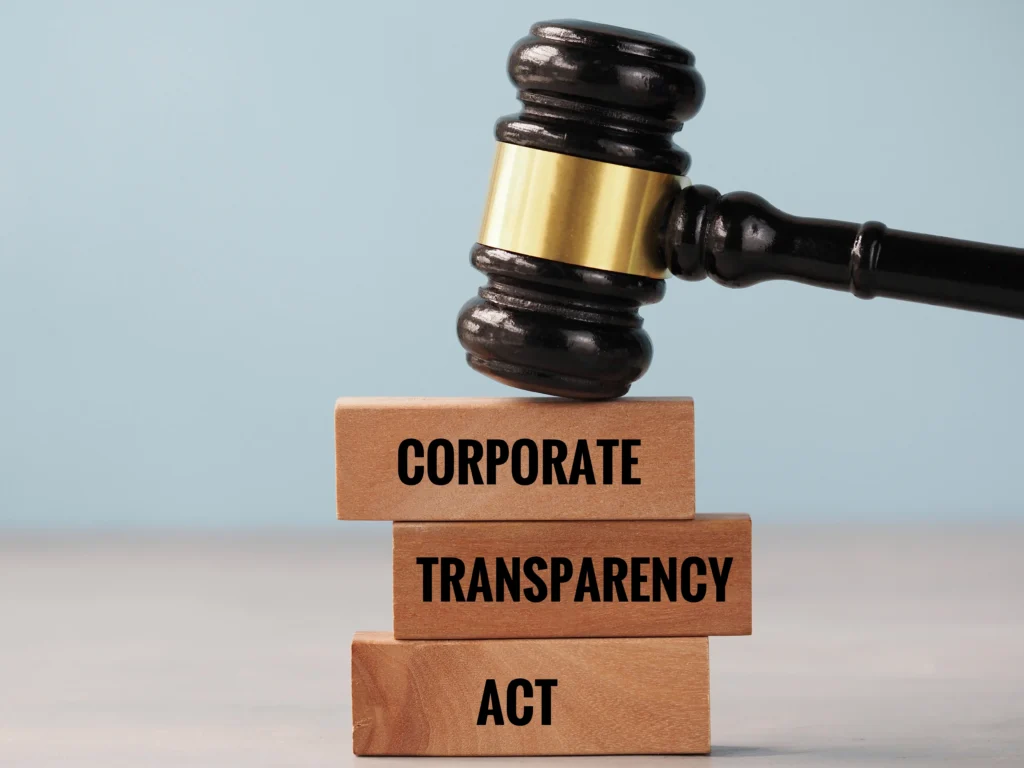 Wooden judge's gavel resting on stacked blocks labeled "Corporate Transparency Act" against a light blue background.