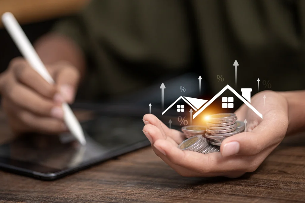 Hand holding stacked coins with digital house icons and percentage symbols above.