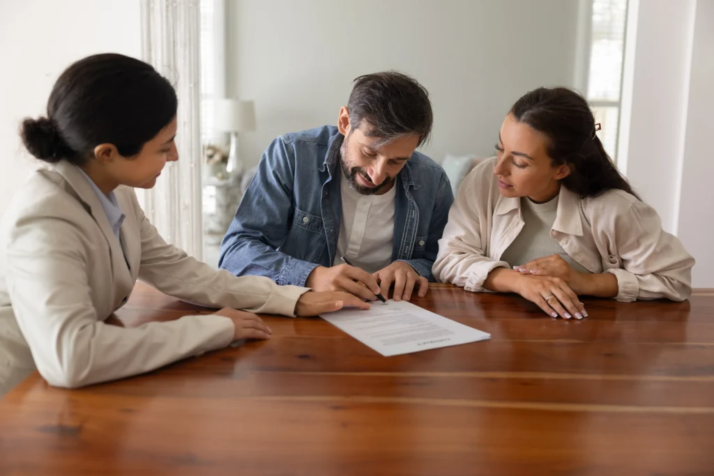 Three adults seated at a wooden table, a man signing a document labeled "LEASE AGREEMENT.