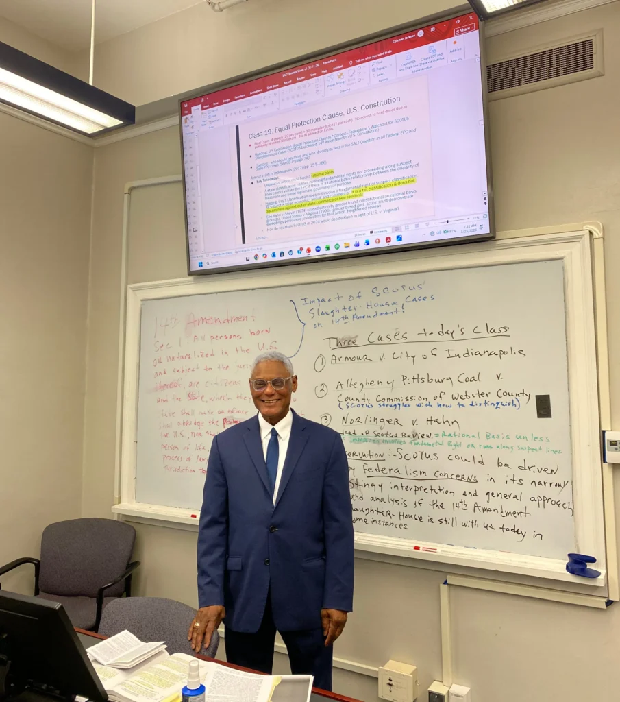 Professional man in blue suit standing in classroom with whiteboard and legal lecture slide.