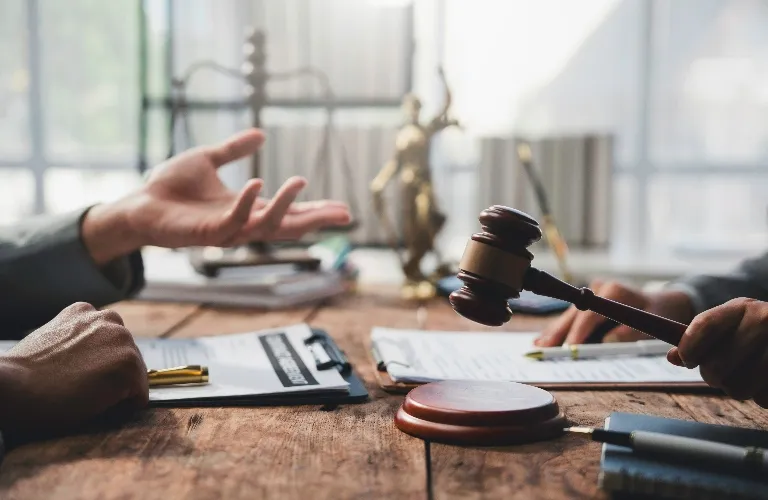 Two individuals at a wooden table with legal documents, a gavel, and a statue of Lady Justice.