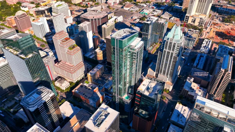Aerial view of a downtown cityscape with skyscrapers, modern glass buildings, and streets in sunlight.