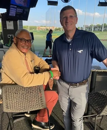 Two men shaking hands at an outdoor golf driving range during daytime.