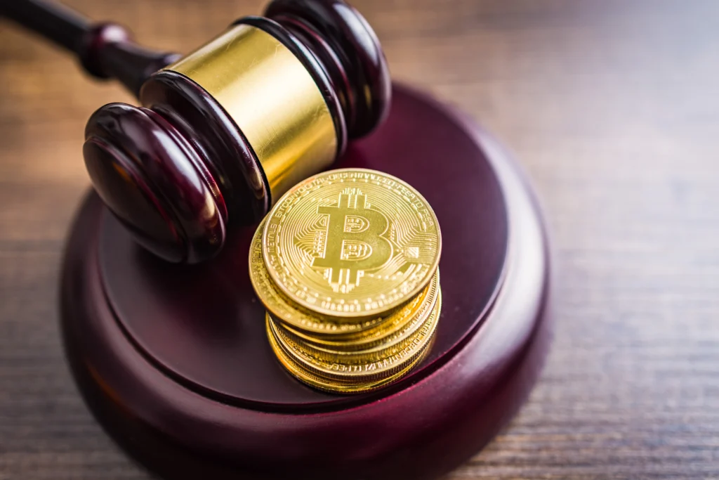 Stack of gold Bitcoin coins beside wooden judge gavel on desk.