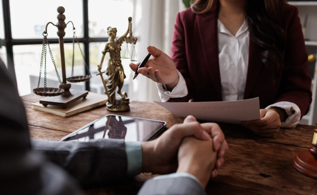 Professional consultation scene with female lawyer reviewing documents, scales of justice, and tablet on wooden desk.