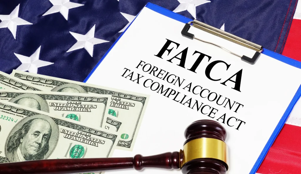 Clipboard with FATCA Foreign Account Tax Compliance Act text, US dollar bills, gavel, and American flag background.