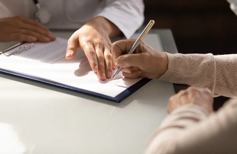 Two people at a table, one signing a document on a clipboard while the other observes.