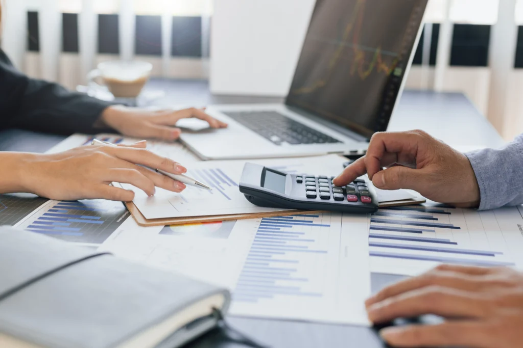 Close-up of two professionals analyzing financial charts with a calculator and laptop on desk.