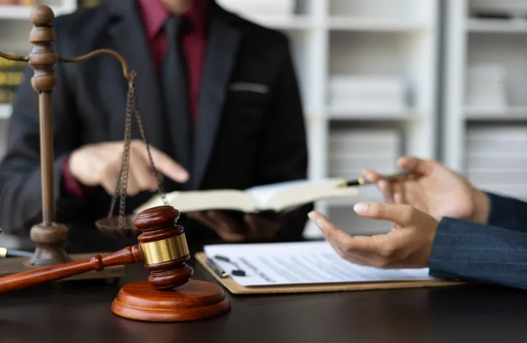 Two professionals in formal attire discussing legal documents with gavel and scales of justice on table.