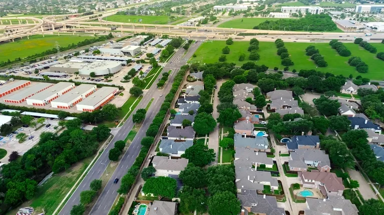 Aerial view of residential neighborhood with houses, trees, roads, and a nearby highway interchange.