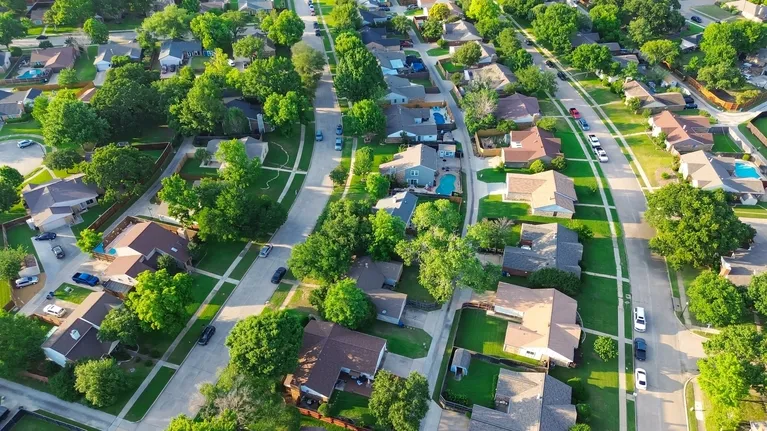 Aerial view of a suburban neighborhood with houses, green lawns, trees, and curved streets.