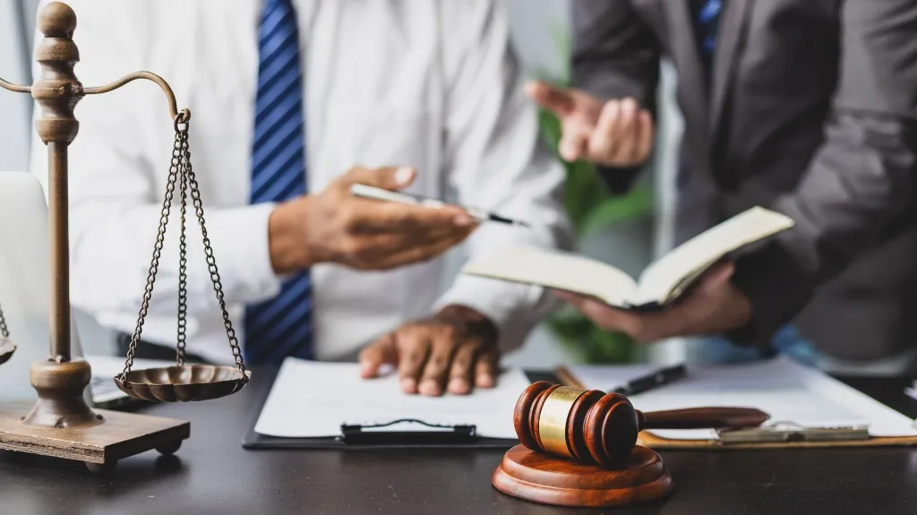 Two professionals discussing legal documents with scales of justice and gavel on desk.