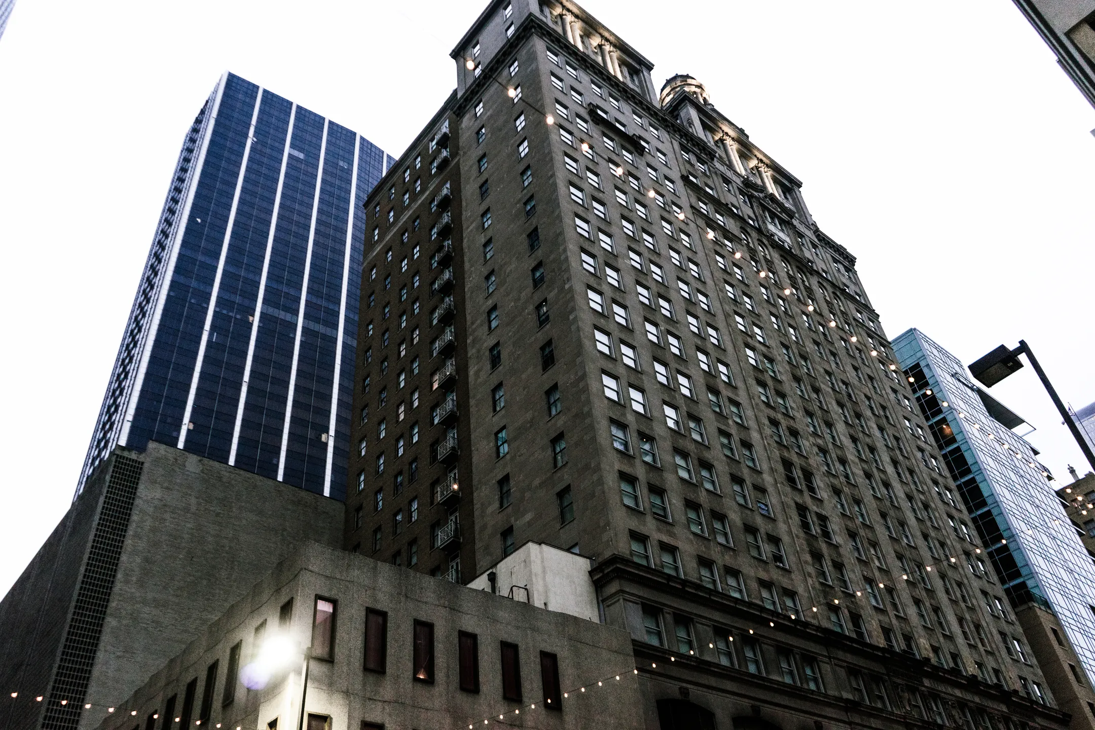 Low-angle view of tall urban buildings with glass and stone facades against a bright sky.