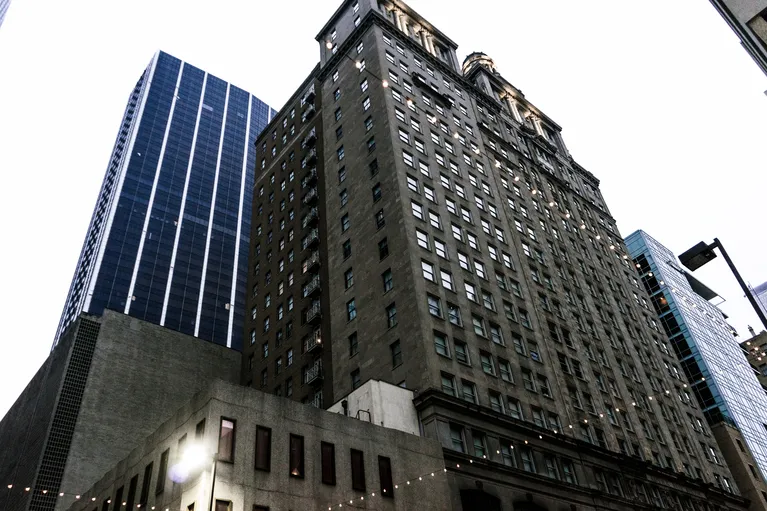View of tall urban buildings with numerous windows under overcast sky, including a dark blue glass skyscraper.