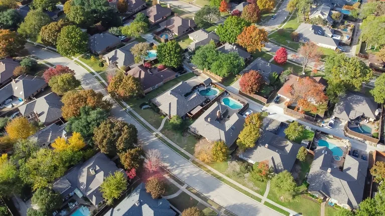 Aerial view of a suburban neighborhood with houses, swimming pools, and autumn-colored trees.
