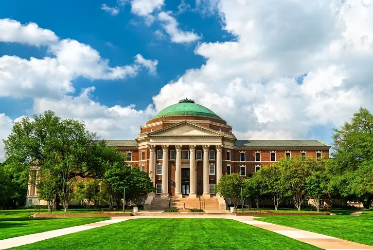 Neoclassical red brick building with green dome, tall columns, surrounded by trees and lawn.