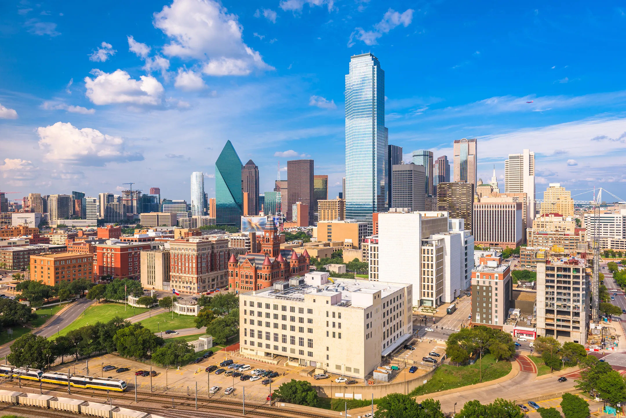 Panoramic view of Dallas skyline featuring modern skyscrapers, historic buildings, and a blue sky.