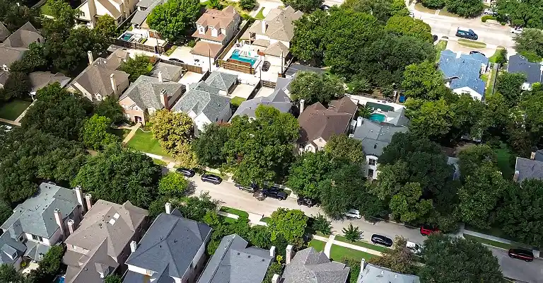 Aerial view of a residential neighborhood with houses, trees, and parked cars along the street.