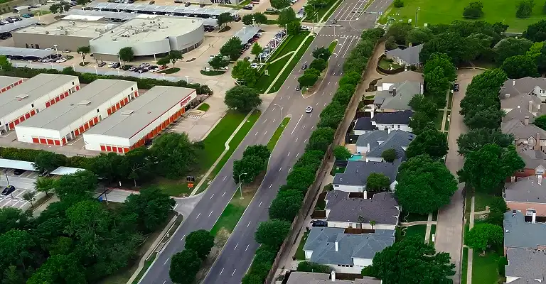 Aerial view of a suburban neighborhood with houses, trees, and a multi-lane road.