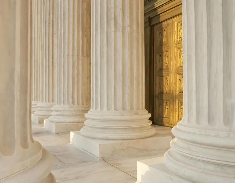 Close-up view of tall white marble columns with fluted shafts beside an ornate golden door.