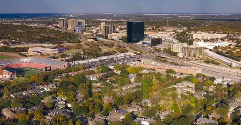 Aerial view of a suburban neighborhood with dense trees, a sports stadium, and city buildings in the background.