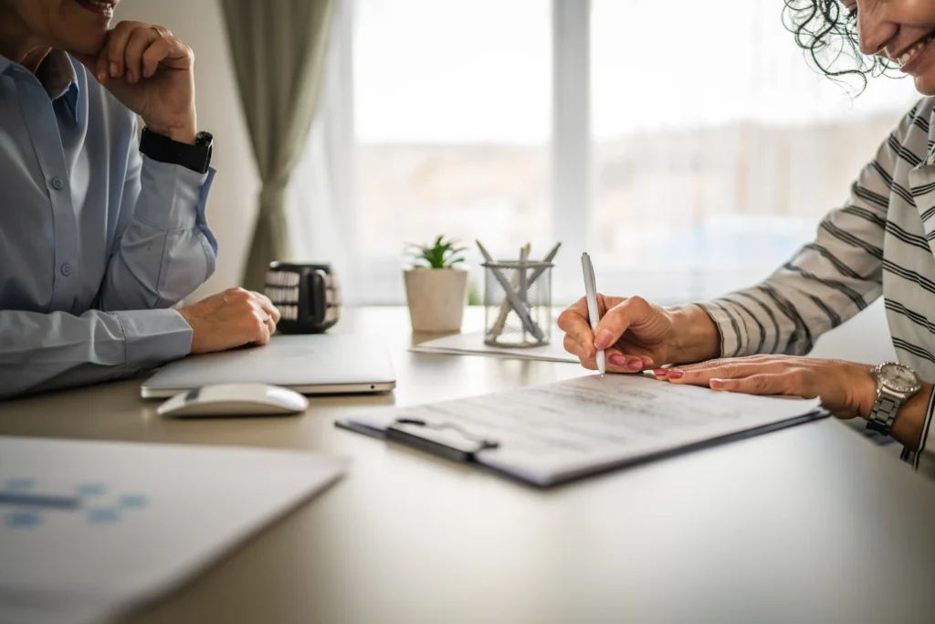 Two professionals at a desk reviewing and signing documents with office supplies visible.