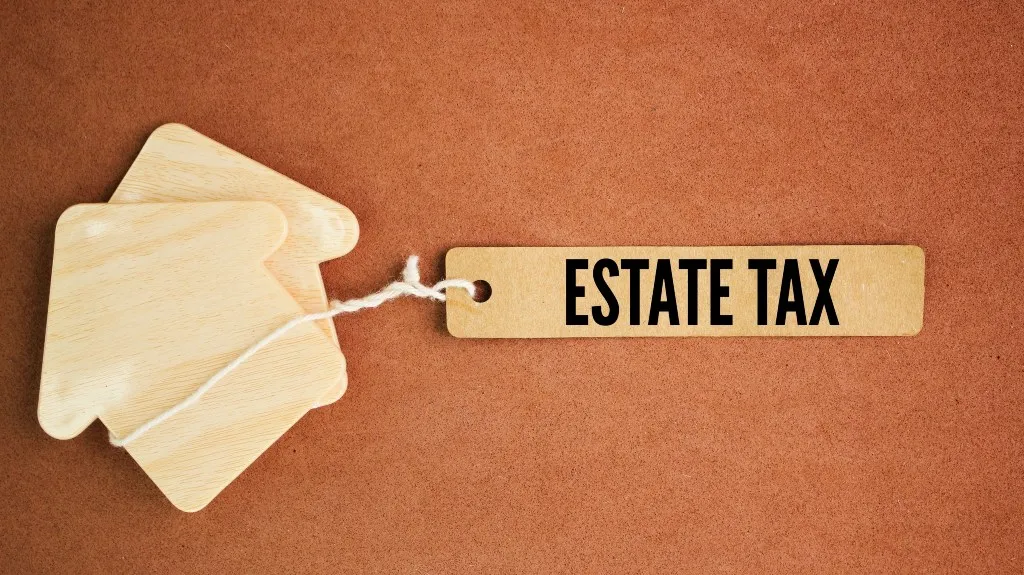 Wooden house-shaped cutouts attached to a tag labeled "ESTATE TAX" on a brown background.