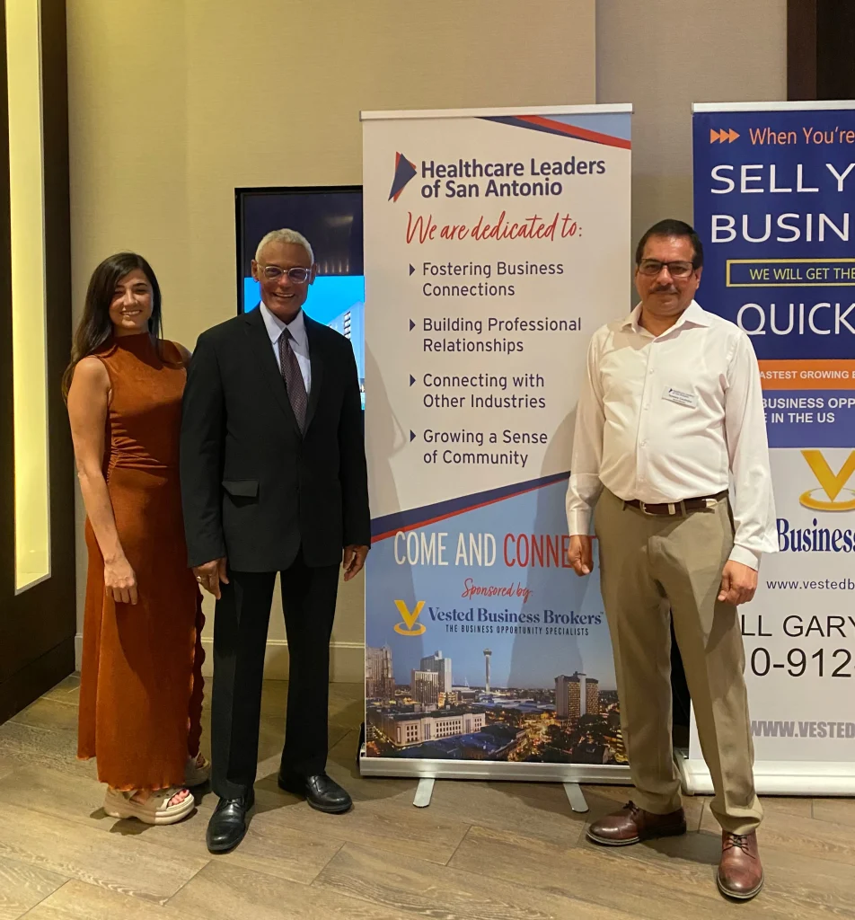Three professionals standing beside Healthcare Leaders of San Antonio and Vested Business Brokers promotional banners.