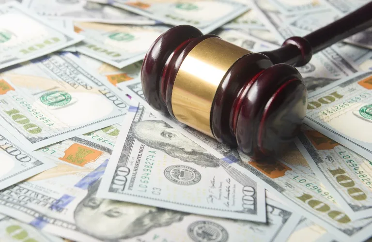 Wooden judge's gavel with brass band resting on scattered US hundred-dollar bills.